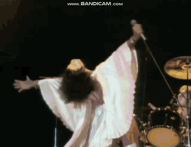 a woman in a white dress is singing into a microphone while dancing on stage .