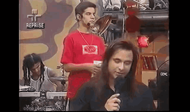 a man with long hair is holding a microphone in front of a drummer .