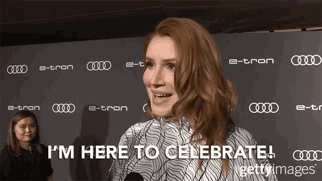 a woman says " i 'm here to celebrate " while standing in front of an audi banner