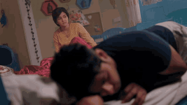 a woman sits on a bed next to a man who is sleeping