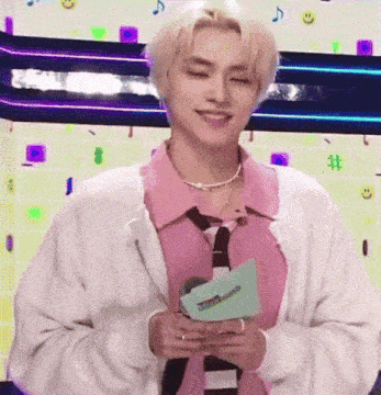 a young man wearing a pink shirt and tie is holding a piece of paper in his hands .