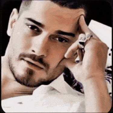 a man with a beard and a ring on his finger is laying down with his hand on his forehead .