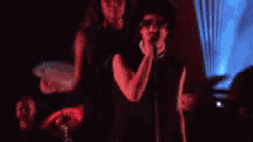 a man in a black shirt is singing into a microphone while dancing on a stage .