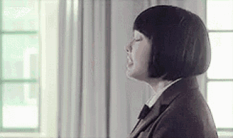 a woman in a suit and bow tie is standing in front of a window with her eyes closed .