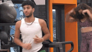 a man is running on a treadmill while a woman looks on .