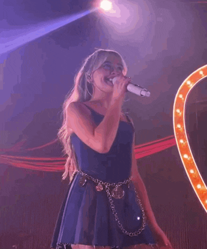 a woman singing into a microphone with a heart in the background