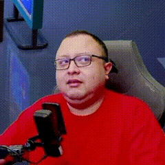 a man wearing glasses and a red sweater is sitting in a chair with a microphone .