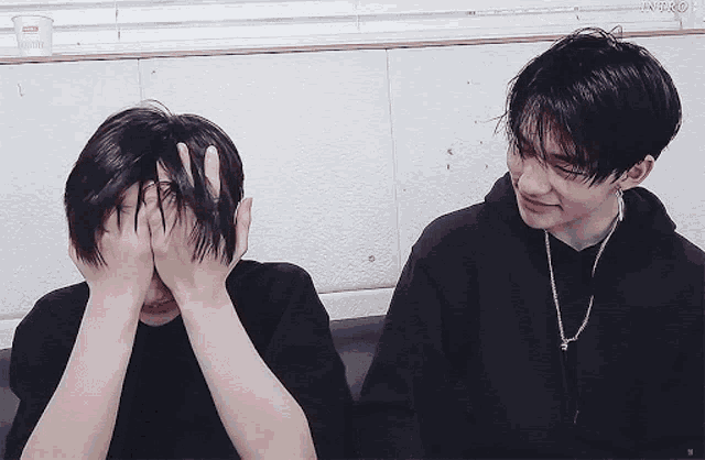 two young men are sitting next to each other and one of them is covering his face with his hands