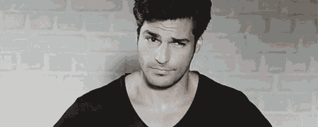 a man wearing a black shirt is making a funny face in front of a brick wall .