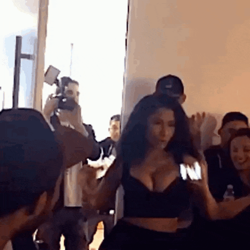a woman in a black crop top is dancing in a room with a group of people .