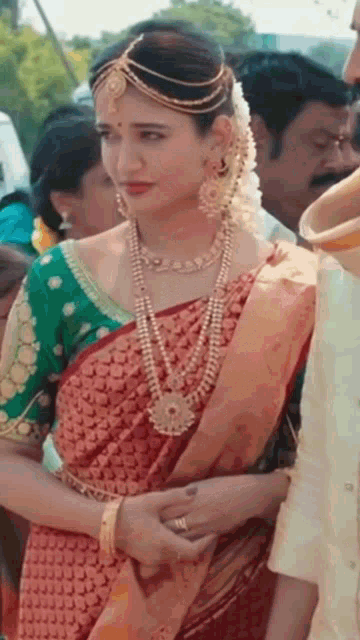 a bride in a red saree and a green blouse is standing next to a man in a white shirt .