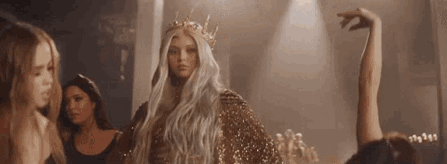 a woman with long white hair and a crown is standing in front of a crowd .