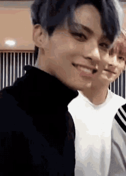 two young men are standing next to each other and smiling . one of the men has blue hair .