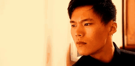 a young man in a black shirt is leaning against a wall and looking at the camera .
