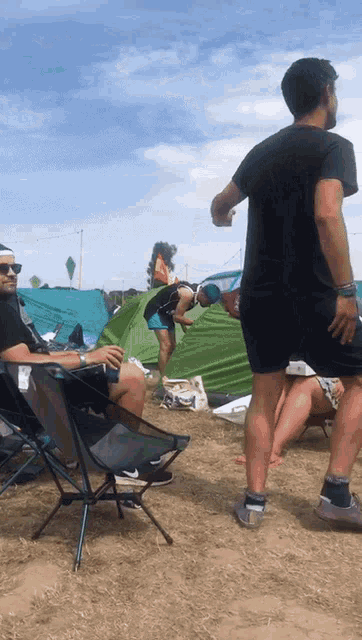 a man in a black t-shirt stands in front of a green tent