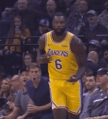 a basketball player wearing a yellow lakers jersey is standing in front of a crowd of people .