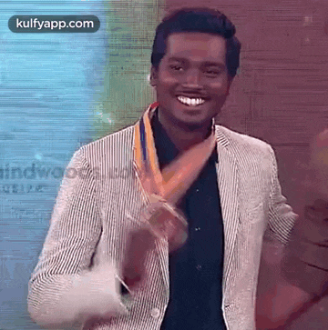a man in a striped jacket is holding a gold medal around his neck and smiling .