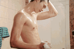 a shirtless man is taking a shower and holding a soap bar