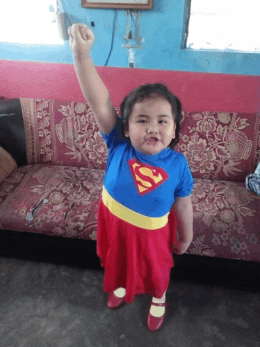 a little girl in a superman costume holds her fist up