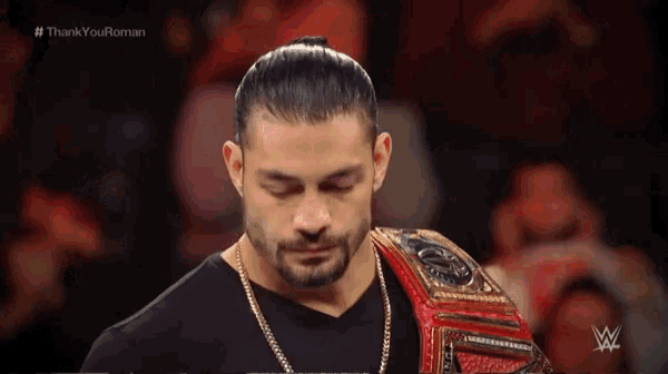 roman reigns is wearing a wwe world heavyweight championship belt while standing in front of a crowd .