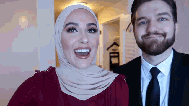 a woman wearing a hijab and a man in a suit smile for the camera