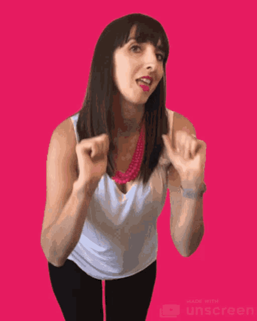 a woman wearing a white tank top and a pink necklace stands in front of a pink background
