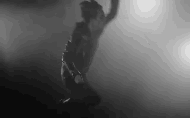 a black and white photo of a man jumping in the air in the fog .