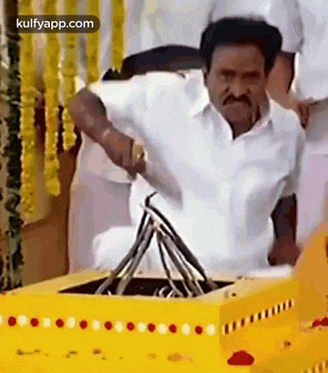 a man in a white shirt is sitting in a yellow box holding a knife .