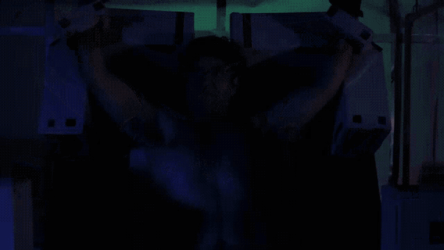 a man without a shirt is in a dark room with a blue light behind him