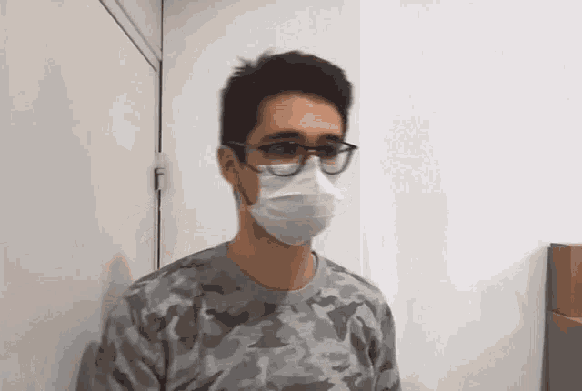 a man wearing a face mask and glasses is standing in front of a door .