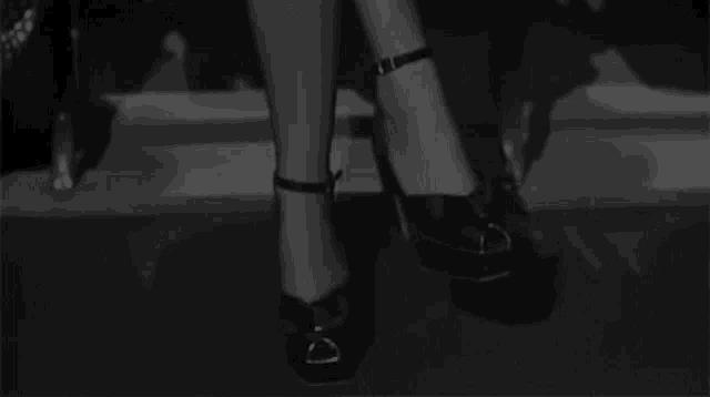 a black and white photo of a woman 's feet wearing heels with a buckle around the ankle .
