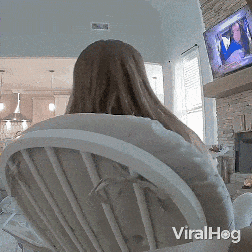 a woman is sitting in a rocking chair in front of a television with the words viralhog on the bottom right