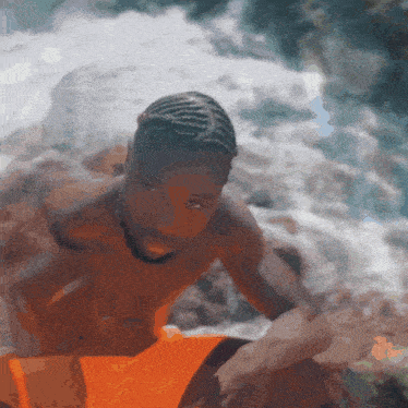 a shirtless man in orange swim trunks sits on a rock