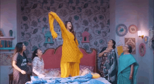 a woman in a yellow dress is standing on a bed surrounded by other women