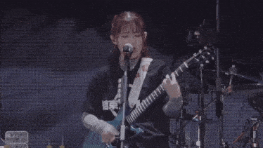 a woman is singing into a microphone while playing a guitar on stage .