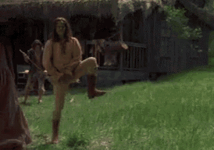 a man and a woman are standing in a grassy field in front of a hut .
