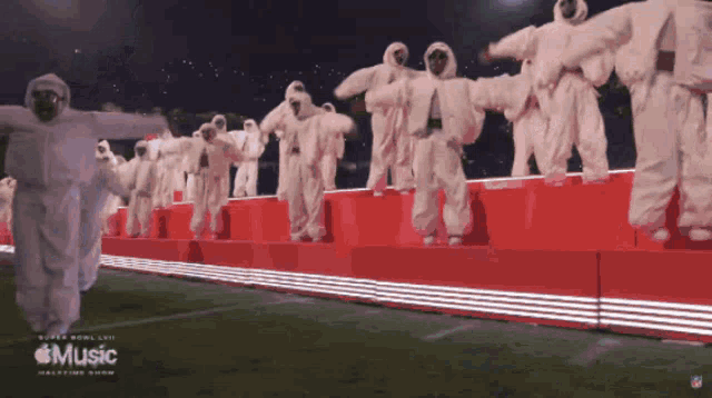 a group of people in white jumpsuits are dancing on a stage that says music on it