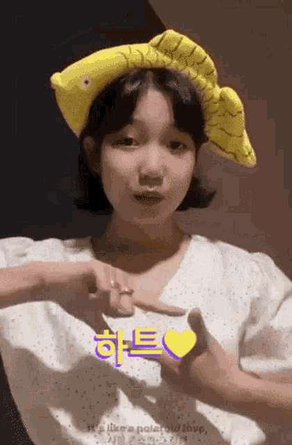 a girl wearing a yellow fish hat making a heart shape with her hands