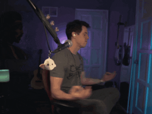 a man sits in front of a microphone in a dark room with a guitar in the background