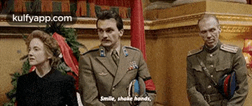 three men in military uniforms are standing next to each other in a room . one of the men is talking to a woman .