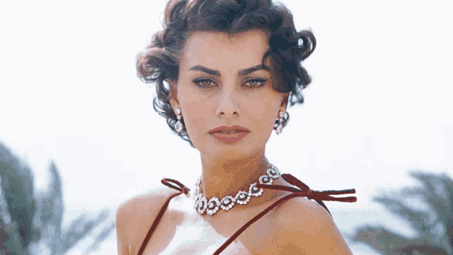 a woman wearing a red dress and a diamond necklace looks at the camera