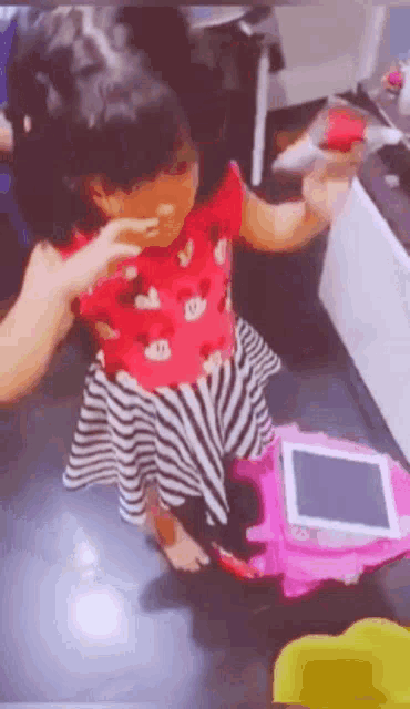 a little girl in a minnie mouse dress is standing next to a pink toy