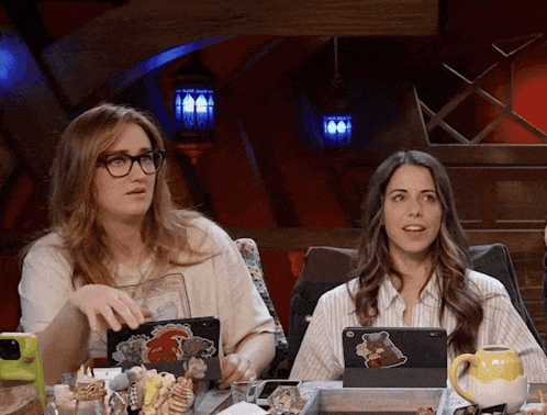 two women are sitting at a table with their laptops and one has a sticker of a bear on it
