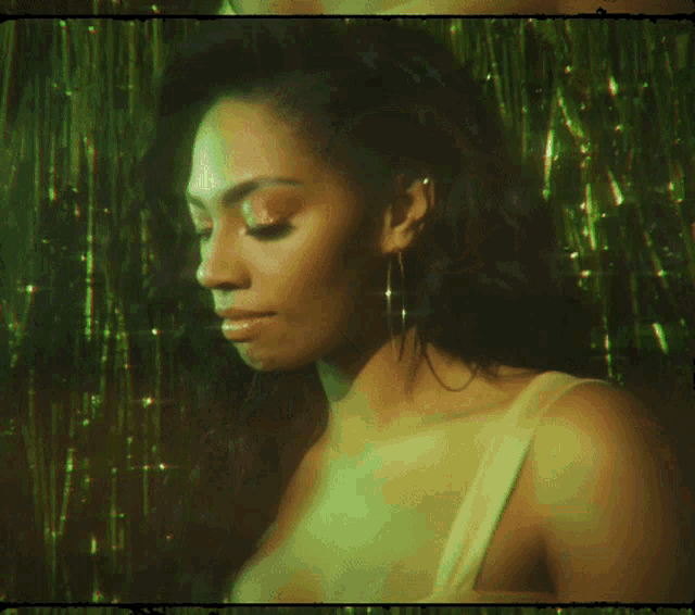 a woman wearing hoop earrings is smiling in front of green tinsel