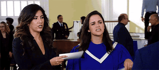 two women are standing next to each other in a room and one is wearing a blue gown .
