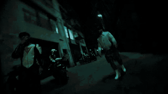 a man wearing a green shirt and a white jacket is walking down a dark street