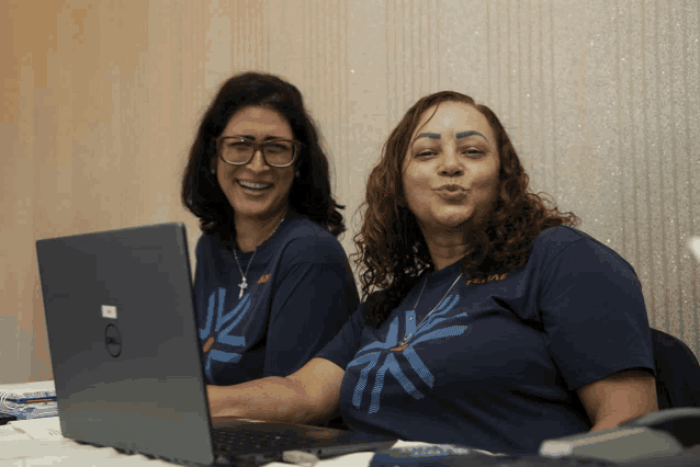 a woman wearing a shirt that says felipe is sitting next to another woman wearing a dell laptop