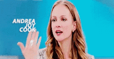 a woman is waving her hand in front of a blue background with andrea joy cook written on it .