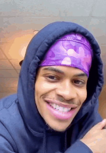 a man wearing a purple headband and a hoodie is smiling .