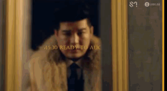 a man in a fur coat and tie is standing in front of a gold frame .